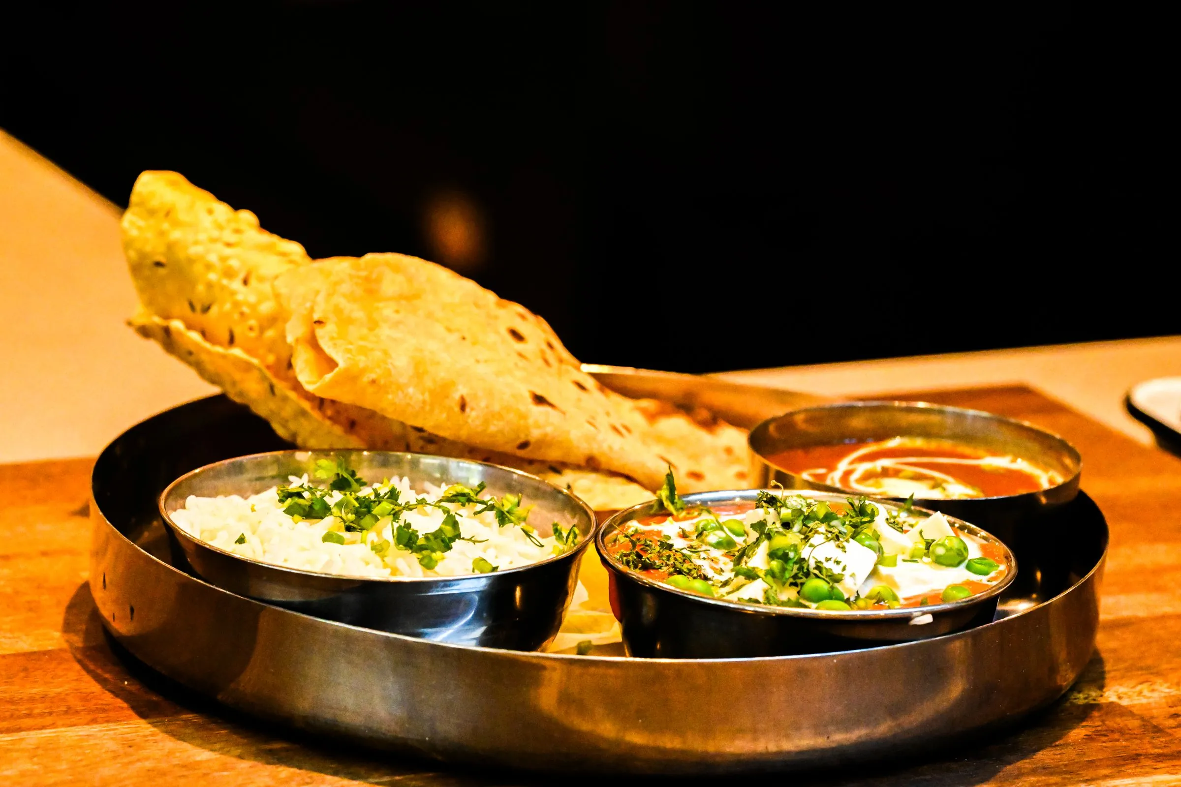 A thali with paneer curry, rice and naan on a wooden table